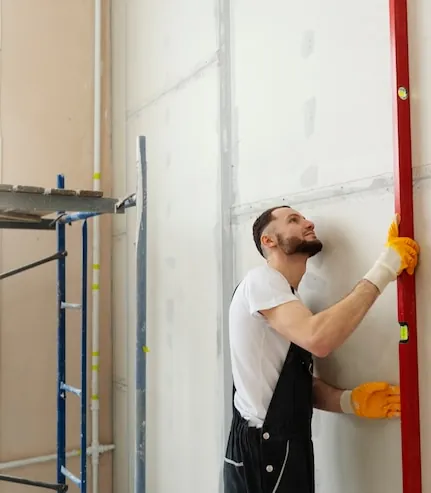 Meseriaș care verifică cu nivela un perete de gips-carton într-un apartament în reparație